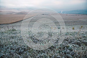 Grass with frost in a field at dawn. Dawn in autumn field. Hills in morning haze. Grass covered with autumn hoarfrost.