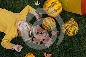 on the grass lies a boy, a bright yellow pumpkin, fallen multi-colored leaves