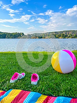 Grass river beach in the Czech Republic, beach ball, picnic mat and pink sneakers on a sunny day