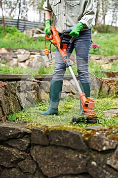 Grass trimmer. Woman is cutting grass next stone wall in garden