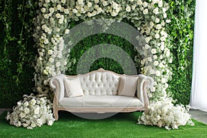 Grass wall wedding backdrop with elegant classic sofa, flowers, candles and lanterns. Luxury decorated blooming wedding photo zone