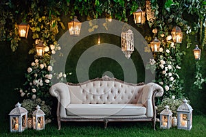 Grass wall wedding backdrop with elegant classic sofa, flowers, candles and lanterns. Luxury decorated blooming wedding photo zone