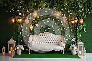 Grass wall wedding backdrop with elegant classic sofa, flowers, candles and lanterns. Luxury decorated blooming wedding photo zone