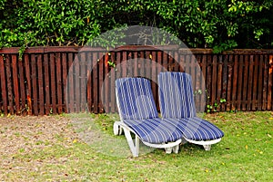 Grassy field with two lounge chairs near a wooden fence