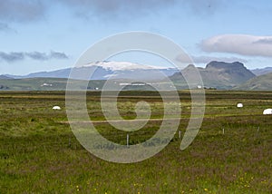 Grassy landscape with mountains and baled hay in meadow near the Black Sand Beach Vik South Iceland