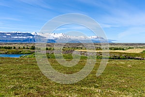 Grassy plain crossed by a river with snow-capped mountains in background