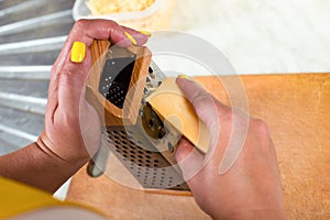 Grate the cheese. Grate Parmesan. Female hands hold a grater. The woman is cooking