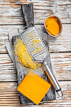 Grated Cheddar Cheese on a wooden cutting board. White wooden background. Top view