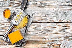 Grated Cheddar Cheese on a wooden cutting board. White wooden background. Top view. Copy space