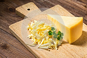 Grated cheese and cheese triangle on cutting board on wooden table