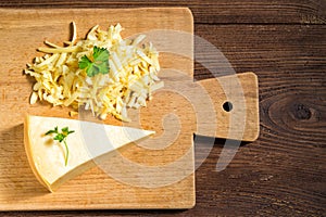 Grated cheese and cheese triangle on cutting board on wooden table