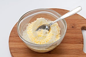 Grated cheese in a crystal bowl on the wooden board with spoon