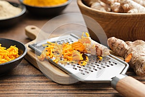 Grated fresh turmeric roots and grater. Bowls of whole and grated curcuma roots, turmeric powder on background.