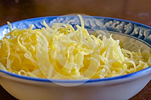 Grated mozzarella and cheddar cheese in dish over wooden background