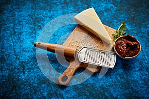 Grated parmesan cheese and metal classic grater placed on wooden cutting board