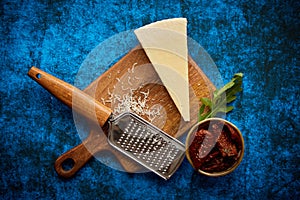 Grated parmesan cheese and metal classic grater placed on wooden cutting board