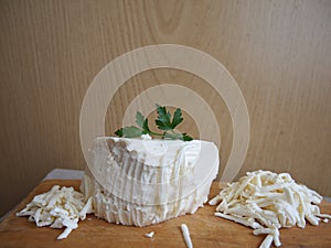 Grated sheep cheese on a wooden board with a branch of parsley
