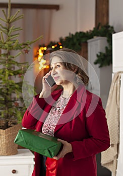 Grateful cheerful Mature woman is talking on the mobile phone while holding a gift box in her hands.