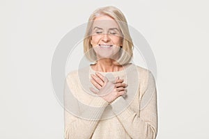 Grateful mature woman holding hands on chest isolated on background photo