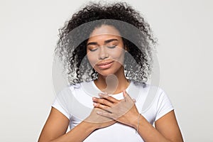 Grateful hopeful African American woman holding hands on chest