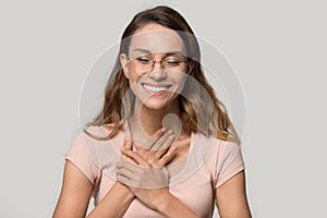 Grateful hopeful young woman wearing glasses holding hands on chest