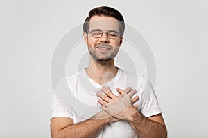 Grateful man in glasses feel thankful keeping hands on chest