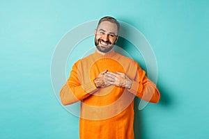 Grateful man smiling, holding hands on heart, thank you gesture, feeling touched with gift, standing over turquoise