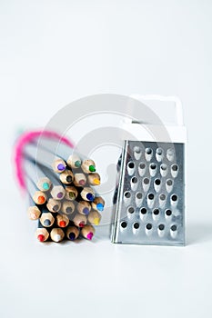Grater with colored pencils on a white background