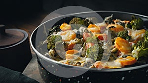 Gratin with broccoli, carrots and cheese baked in the oven on a dark wooden table