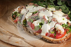 gratinated bread with tomato, spring onions, bacon and mozzarella cheese, quick and easy pizzatoast on baking paper and a rustic