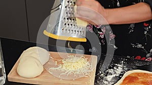 Grating cheese on wooden chopping board. Female hands grate hard cheese for pizza or pasta. Woman cooking delicious dinner for fam