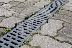 Grating of drainage system rainwater in the park at the sidewalk from a stone shaped paving slabs