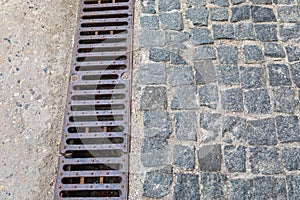Grating of drainage system rainwater in the park at the sidewalk from a stone shaped paving slabs