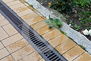 Grating of drainage system rainwater in the park at the sidewalk from a stone yellow paving slabs