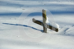 Grave with wooden cross in deep snow in winter