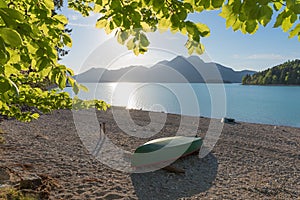 Gravel beach lake Walchensee with boat, evening sun, view through green beech leaves