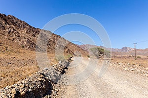 Gravel dirt road through rocky limestone Hajar Mountains and cliffs in United Arab Emirates