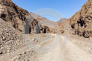 Gravel dirt road through rocky limestone Hajar Mountains and cliffs in United Arab Emirates, barren desert vegetation