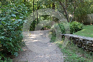 Gravel path leading to a crest in the road, bordered by vegetation, retaining wall, and grass