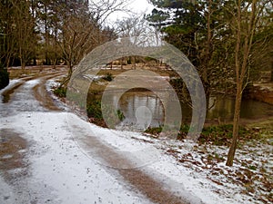 Gravel road covered in snow next to a pond