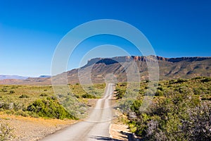 Gravel road crossing the majestic landscape at Karoo National Park, travel destination in South Africa.