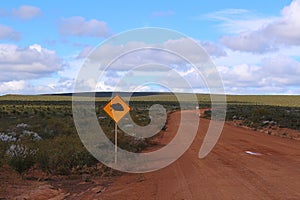 Gravel road with echidna wildlife traffic warning sign in the Western Australian outback