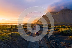 Gravel road at sunset with Vestrahorn mountain and a car driving, Iceland