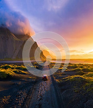 Gravel road at sunset with Vestrahorn mountain and a car driving, Iceland