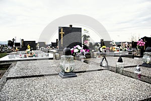 Graves, tombstones and crucifixes on traditional cemetery. Votive candles lantern and flowers on tomb stones in graveyard