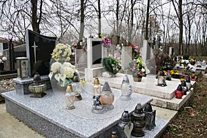 Graves, tombstones and crucifixes on traditional cemetery. Votive candles lantern and flowers on tomb stones in graveyard