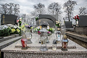 Graves, tombstones and crucifixes on traditional cemetery. Votive candles lantern and flowers on tomb stones in graveyard