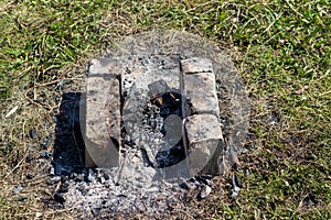 Gray ashes on the ground from a fire with bricks, a barbecue place for frying barbecue and meat in nature, ashes