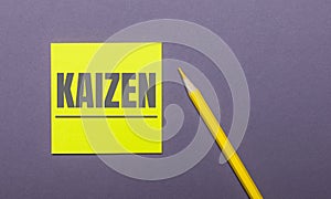 On a gray background, a bright yellow pencil and a yellow sticker with the word KAIZEN