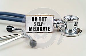 On a gray background, a stethoscope and a cardboard sign with the inscription - Do not self-medicate